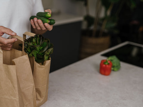 Personne sortant des légumes de sacs de courses en papier, sur un plan de travail de cuisine
